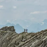 Two hikers crossing a rocky ridge high in the mountains, one a step ahead