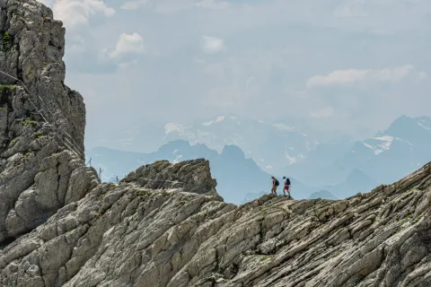 Two hikers crossing a rocky ridge high in the mountains, one a step ahead