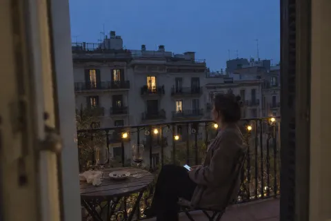 A woman sitting alone on a city balcony in the evening, her phone in her lap