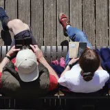 Two people side by side on a bench, each on their own phone, seen from above