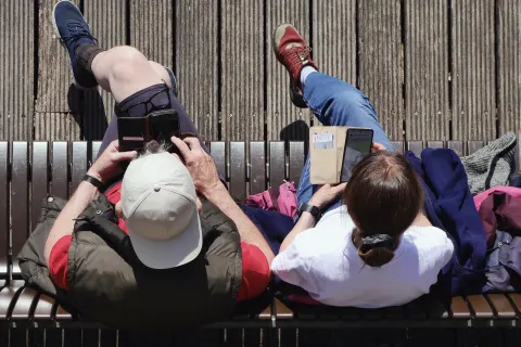Two people side by side on a bench, each on their own phone, seen from above