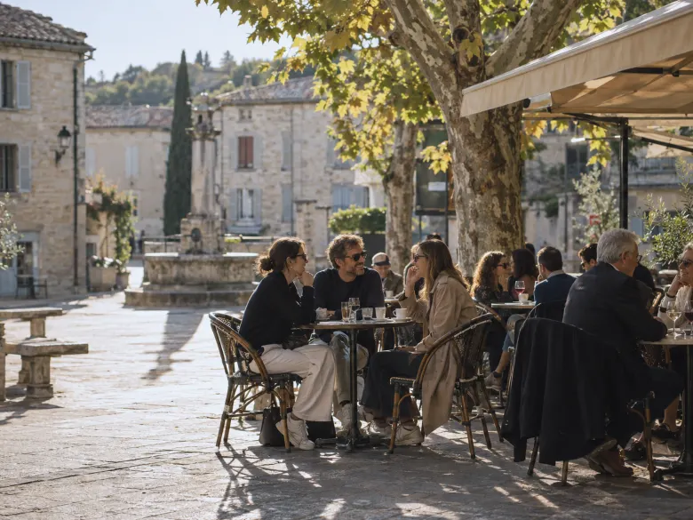 People talking at small tables on a café terrace on a town square in late afternoon sun