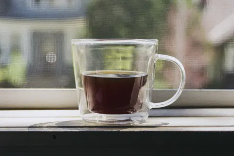 A glass mug of coffee on a sunny windowsill, a quiet street of wooden houses outside