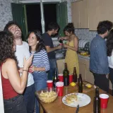 Friends talking and laughing in a small, crowded kitchen at a house party