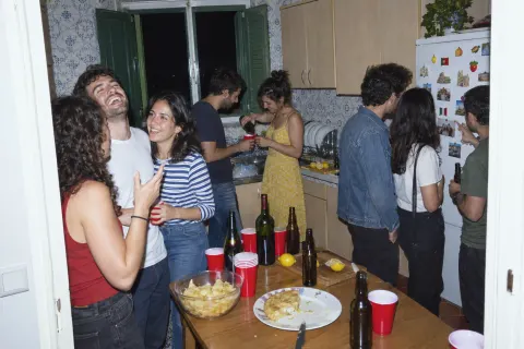 Friends talking and laughing in a small, crowded kitchen at a house party