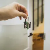 A hand holding a bunch of keys by an open white door