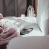 A phone lying on rumpled pink bed sheets in daylight