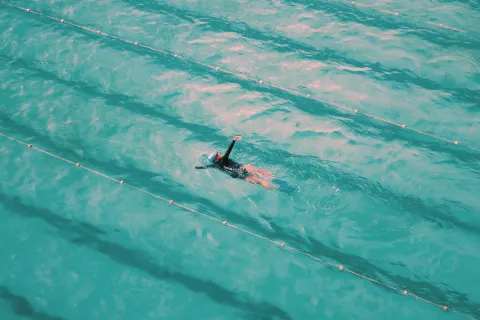 One swimmer doing lengths in a bright turquoise outdoor pool, seen from above