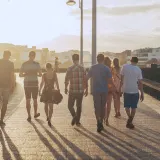 A group of friends walking along a seafront promenade in the evening sun