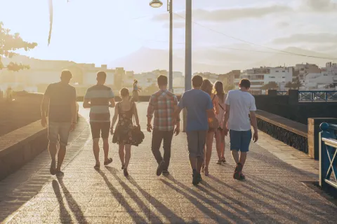 A group of friends walking along a seafront promenade in the evening sun