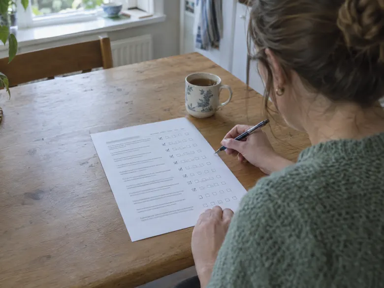 A woman at a kitchen table ticking boxes on a printed questionnaire