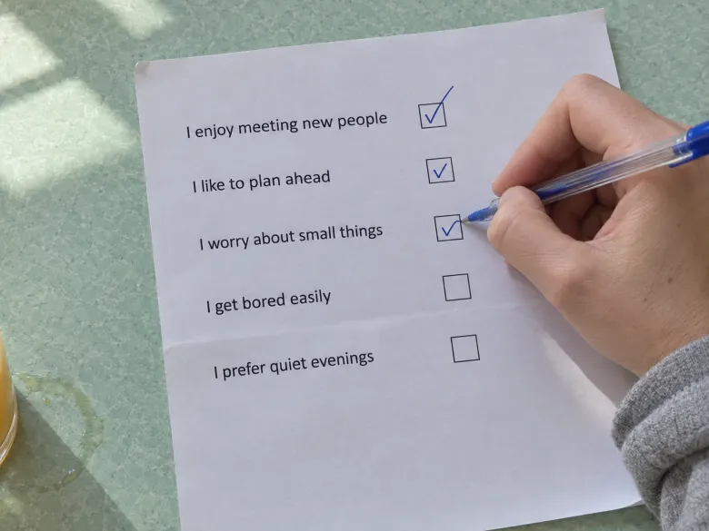 A hand ticking boxes on a printed quiz sheet on a mint green kitchen table