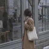 A woman on a rainy shopping street catches her own reflection in a shop window