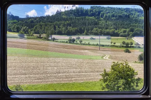 Green fields and a wooded hill seen through a train window on a sunny day